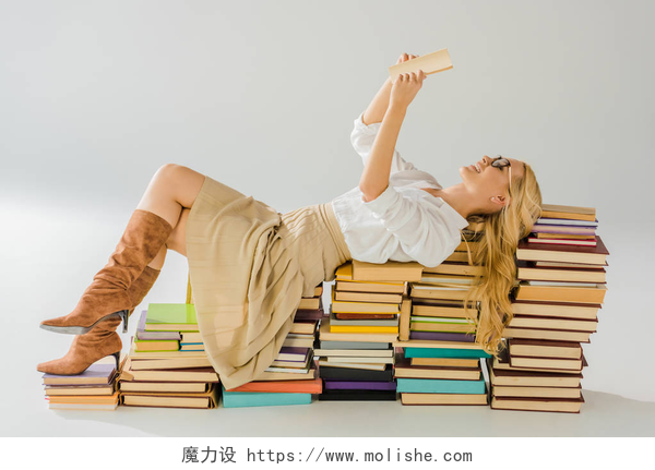 白色的背景下一个女人躺在书籍上看书美丽的金发碧眼的女人在眼镜阅读和奠定了一堆复古书籍